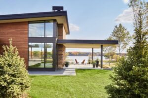 a modern style home with large windows and expansive covered porch overlooking a lake